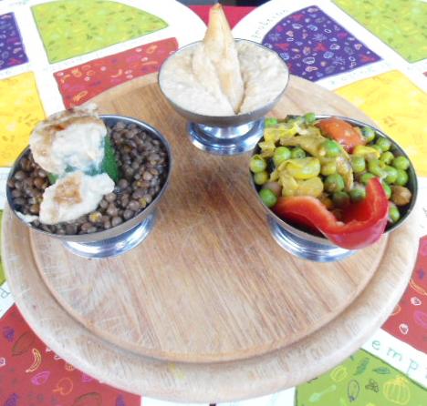 Piatto Alhambra: lenticchie nere, hummus e verdure speziate serviti su tagliere di legno
